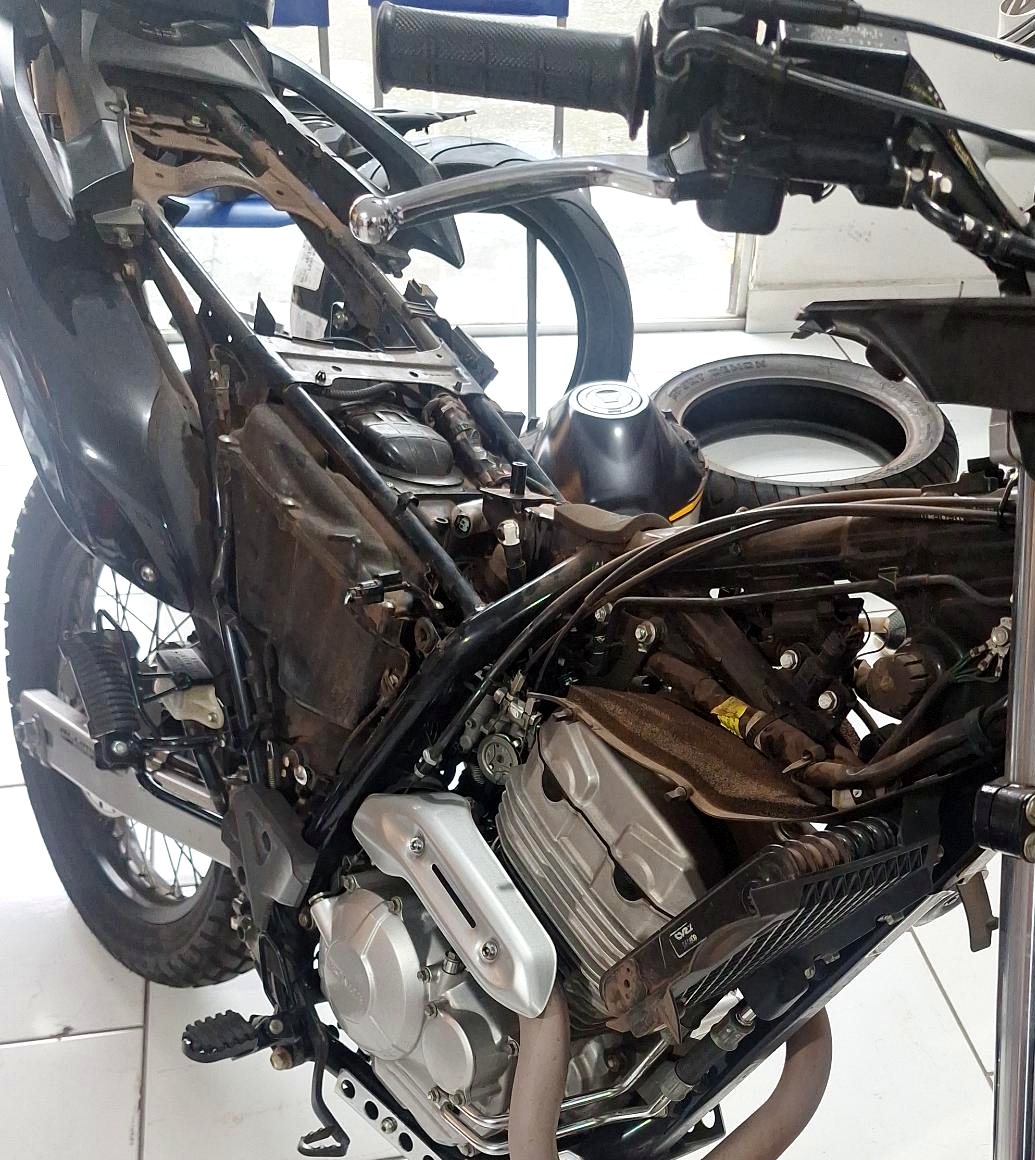 Moto trail com o motor e o chassi à mostra, em manutenção na oficina.